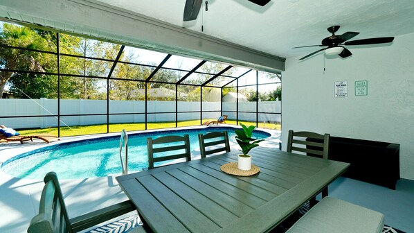 An indoor pool area with a table and chairs, a ceiling fan, and a view of the outdoor pool. - Dog Friendly -4 Bed 2 Bath w/ HTD Pool (Sleeps 13) (Sarasota)