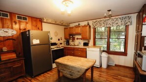 Una cocina con armarios de madera, un refrigerador, una mesa y un ventanal con persianas.