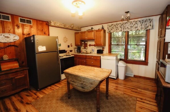 A kitchen with wooden cabinets, a refrigerator, a table, and a window with blinds. - Birchwood Retreat located on private Finely Lake (St Germain)