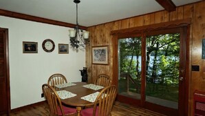 Un comedor con una mesa y sillas de madera, cuadros en la pared y vistas a árboles a través de un ventanal.