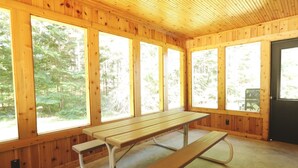 A wooden cabin with a picnic table and large windows.