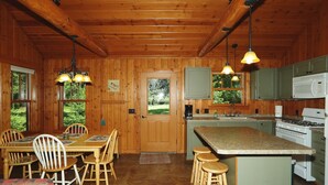 A wooden cabin interior with a dining area, kitchen, and large windows.