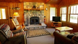 A cozy cabin interior with a stone fireplace, wooden walls, a television, and comfortable seating.