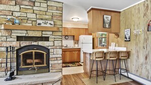 A kitchen with a stone fireplace, wooden cabinets, and a bar area with stools.