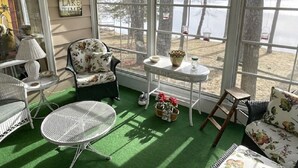 Un solárium con vistas a un lago, amueblado con sillas de mimbre y una mesa.
