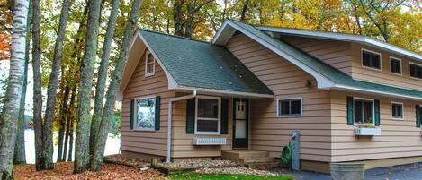A two-story house with a sloped roof, a front porch, and a small front yard with a gravel path and a metal chair.