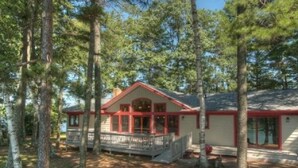 Une cabane dotée d’une véranda, entourée de grands arbres.