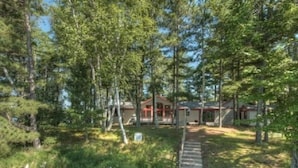 Un bâtiment de style cabane, entouré d’une forêt dense, avec une terrasse en bois menant à l’entrée.