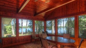 Une cabane en bois avec une table à manger ronde et des chaises, de grandes fenêtres donnant sur une forêt et un lac.