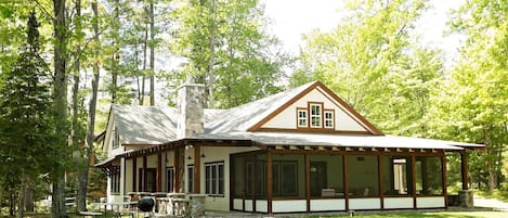 A cabin with a stone chimney, large windows, and a covered porch.