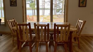 Zona pranzo con tavolo e sedie in legno, una grande finestra vista su un lago e alberi, e un cartello sopra la finestra con la scritta "UP NORTH".