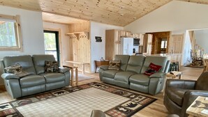 Un ampio soggiorno con divani in pelle, un soffitto in legno e una cucina sullo sfondo.