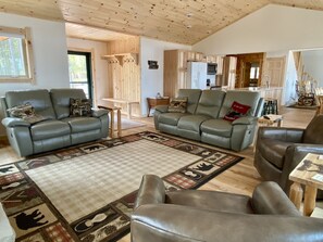 A spacious living room with leather sofas, a wooden ceiling, and a kitchen in the background. - Lakeside Pines located on Pickerel Lake (St Germain)