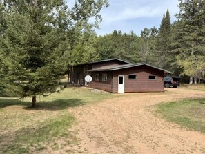 A single-story cabin with a sloped roof, a satellite dish, and a small porch. - Liam's Landing located on Little St Germain Lake (St Germain)