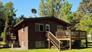 A two-story cabin with a deck, satellite dish, and a small outdoor area. - Liam's Landing located on Little St Germain Lake (St Germain)