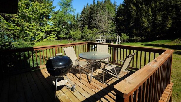 A wooden deck with a table and chairs, a grill, and a wooden railing. - Liam's Landing located on Little St Germain Lake (St Germain)