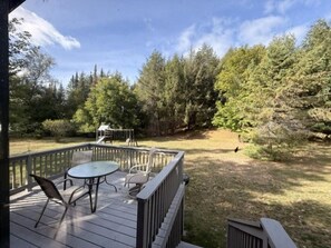 A wooden deck with a table and chairs, surrounded by trees and a grassy area. - Liam's Landing located on Little St Germain Lake (St Germain)