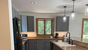 A modern kitchen with grey cabinets, a central island, a window with a view of trees, and a wooden floor. - Eagle Bay on Little St Germain Lake (St Germain)