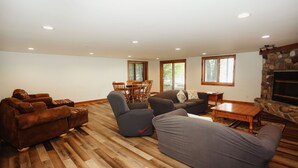 A spacious living room with a fireplace, wooden flooring, and large windows. - Eagle Bay on Little St Germain Lake (St Germain)
