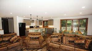 A spacious living room with a large sectional sofa, a kitchen area with modern appliances, and large windows offering a view of the outdoors. - Eagle Bay on Little St Germain Lake (St Germain)