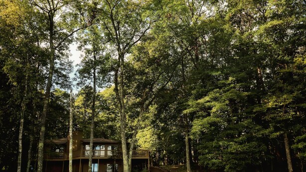 A cabin with a wooden deck and a staircase leading up to it, surrounded by dense forest. - Eagle Bay on Little St Germain Lake (St Germain)