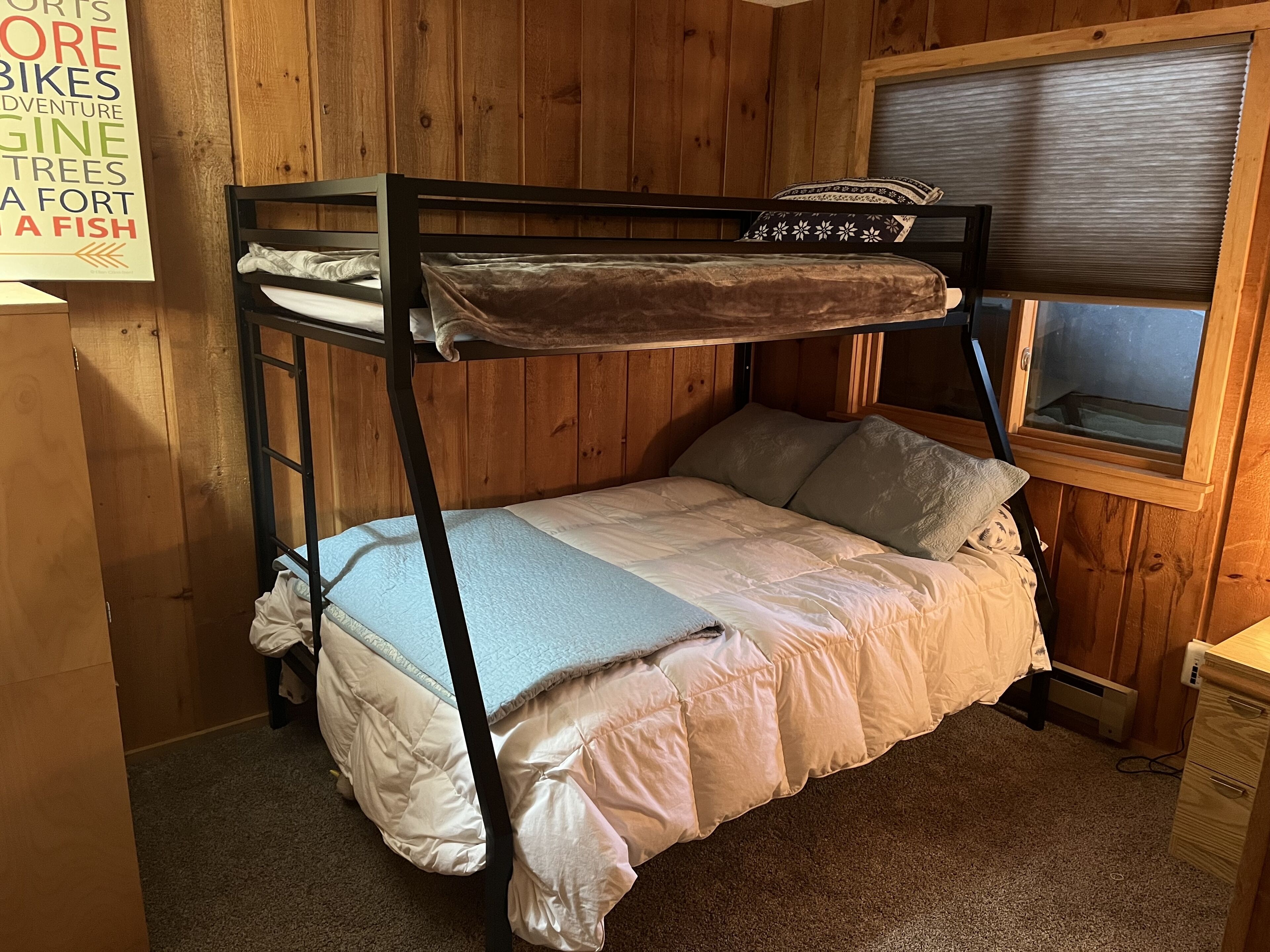 A bunk bed with a window, wooden walls, and a sign on the wall.