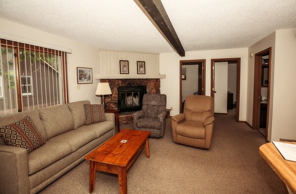 A living room with a sofa, two armchairs, a wooden coffee table, a fireplace, and a stone accent wall.