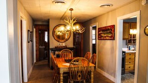 Un coin repas avec une table et des chaises en bois, un lustre et une cuisine en arrière-plan.