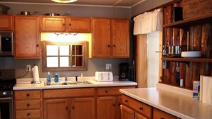 Une cuisine avec des meubles de rangement en bois, un évier, une cuisinière et une fenêtre avec des rideaux.