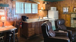 A rustic kitchen with wooden walls, a wooden dining table, a coffee maker, a stove, and two leather chairs. - Deer Run Unit #8 on Big St Germain Lake (St Germain)