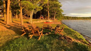 A lakeside setting with wooden chairs arranged on the grass, surrounded by trees and a playground. - Deer Run Unit #9 on Big St Germain Lake (St Germain)