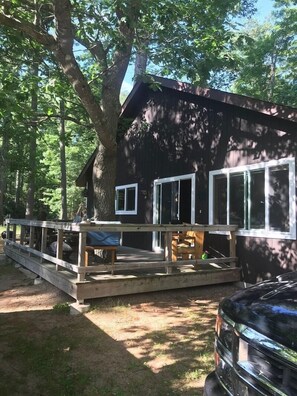 A cabin with a deck, large windows, and a car parked nearby. - Deer Run Unit #10 on Big St Germain Lake (St Germain)