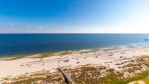 Ein Strand mit Liegestühlen und Sonnenschirmen, einer Holzpromenade und freiem Blick auf das Meer.