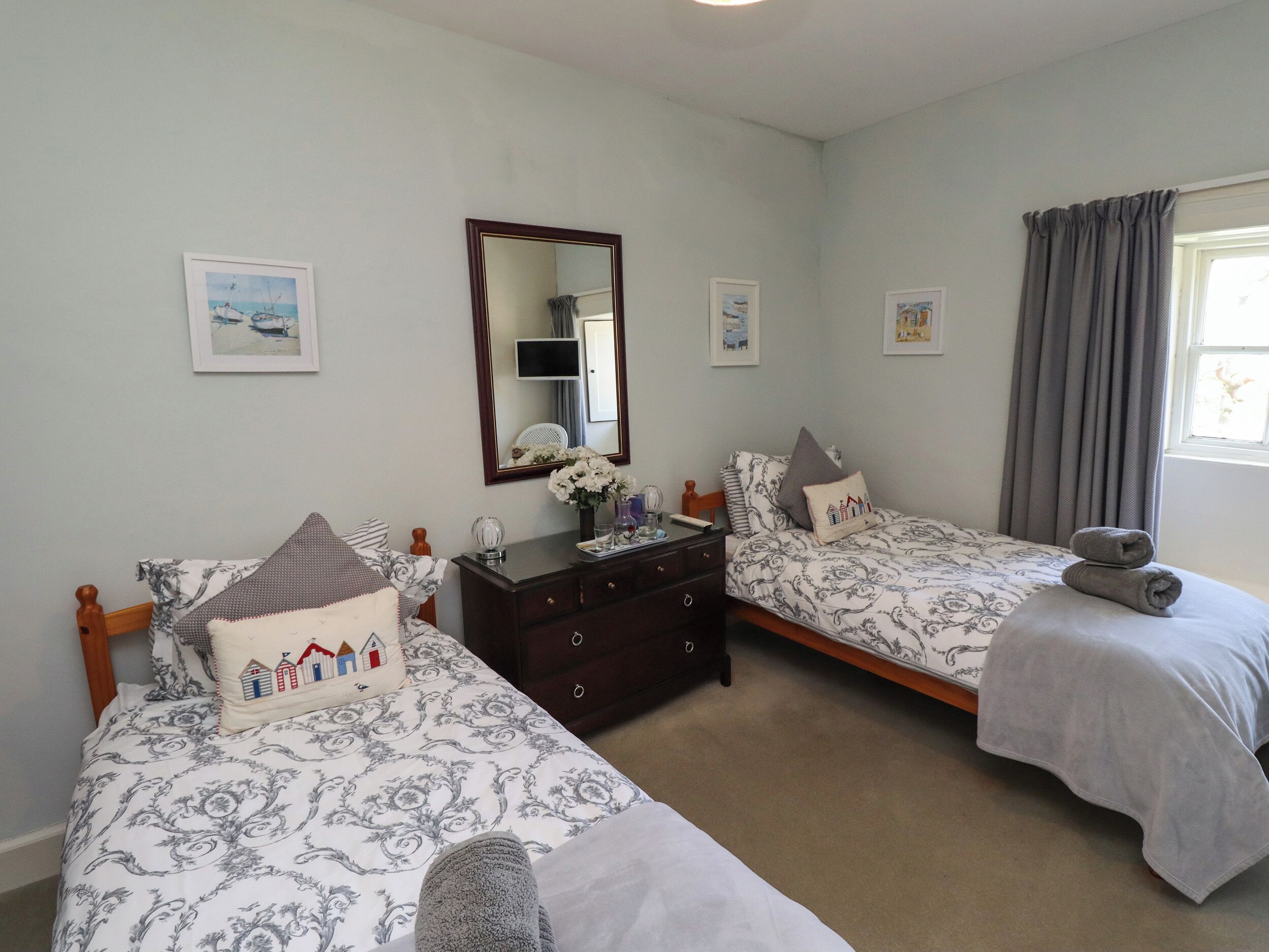A bedroom with two single beds, a dresser, a mirror, and framed pictures on the wall.