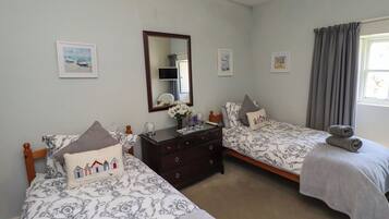 A bedroom with two single beds, a dresser, a mirror, and framed pictures on the wall.
