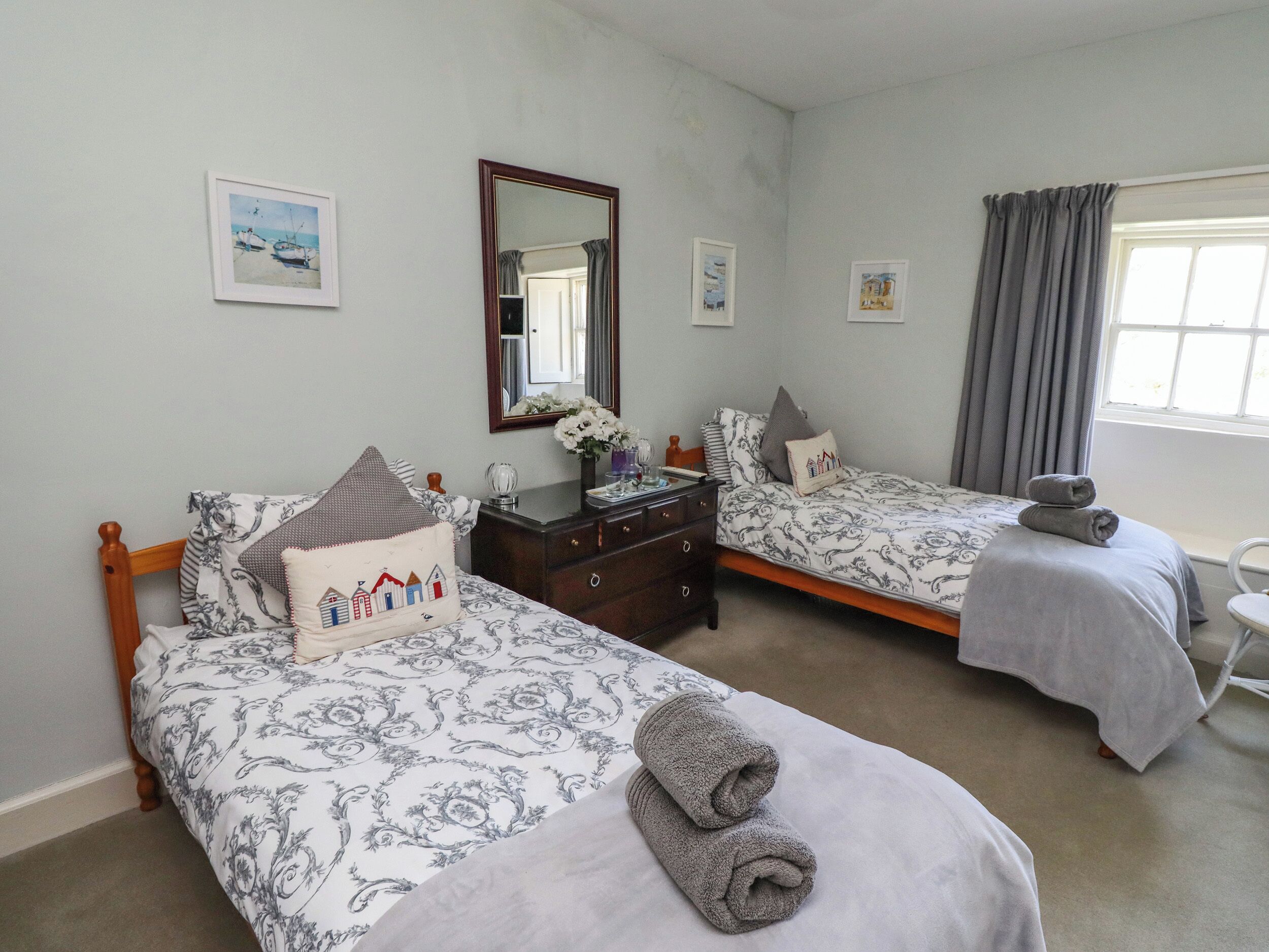 A bedroom with two beds, a dresser, a mirror, and a window with curtains.