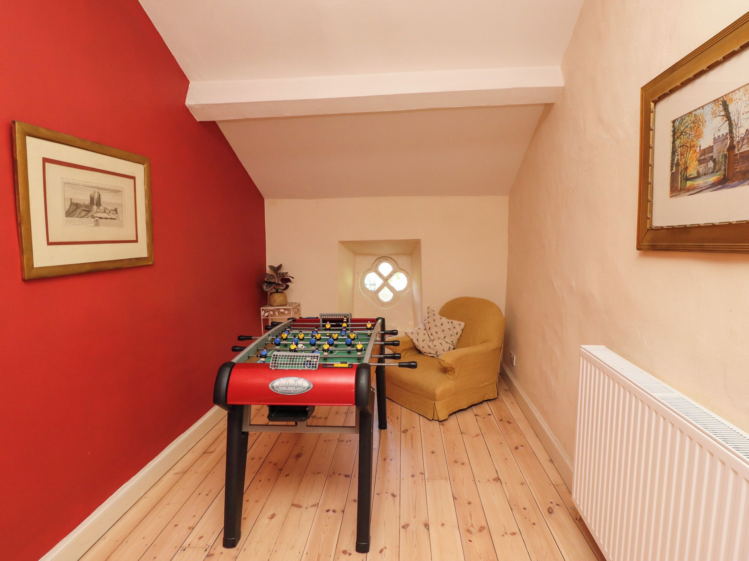 A room with a foosball table, a red wall, a framed picture, and a window with a view.