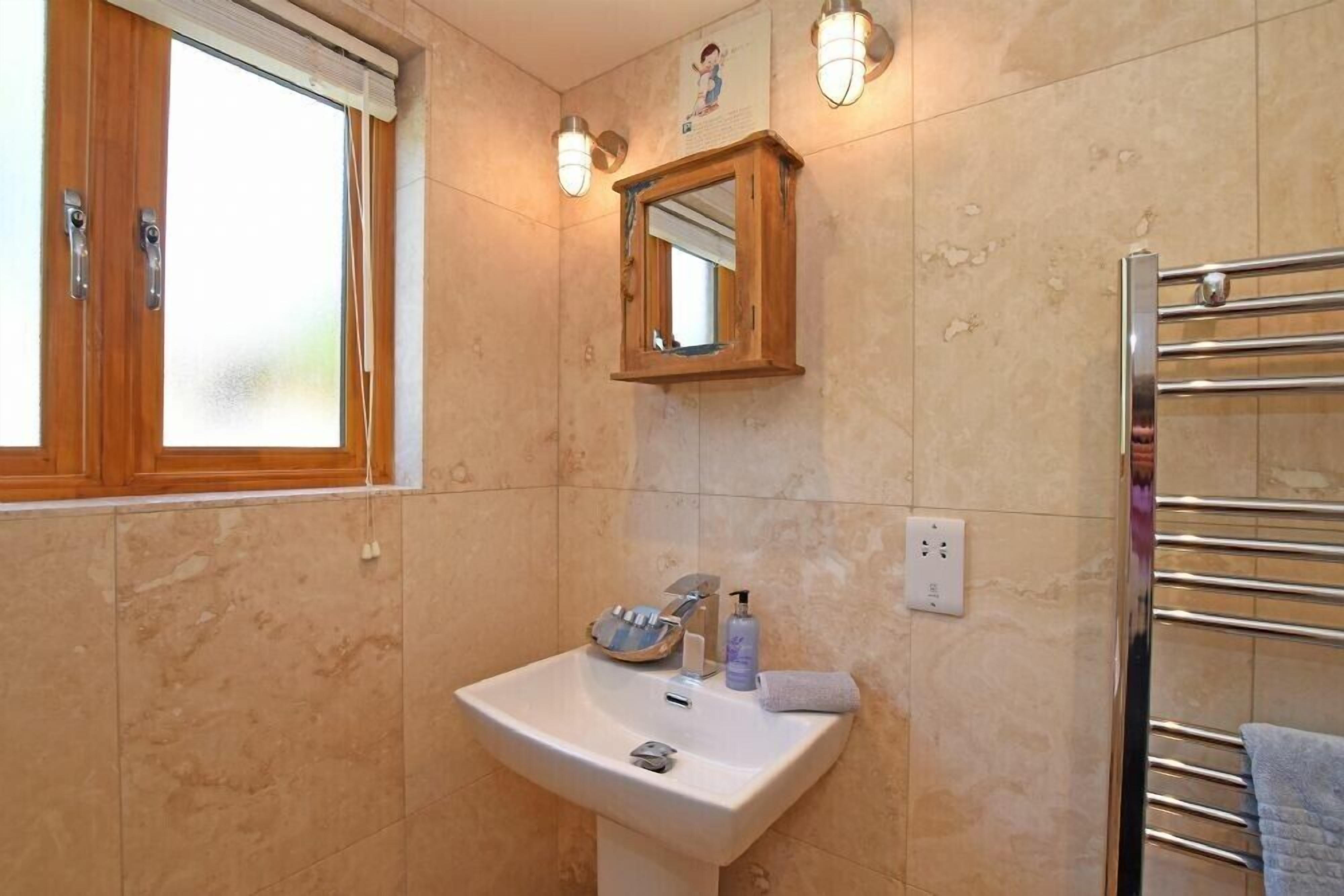 A bathroom with a sink, mirror, towel rack, and a window with wooden frames.