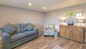 A living room with a grey sofa, a patterned armchair, a wooden cabinet, and a framed picture on the wall. - Dairymaid's Cottage (Morpeth)