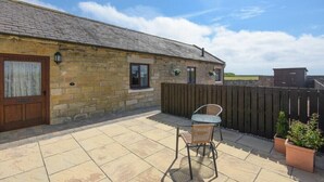 A stone building with a tiled patio, a wooden door, and a window. - Dairymaid's Cottage (Morpeth)