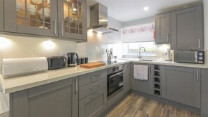 A modern kitchen with grey cabinets, a built-in oven, a microwave, and a coffee maker. - Dairymaid's Cottage (Morpeth)