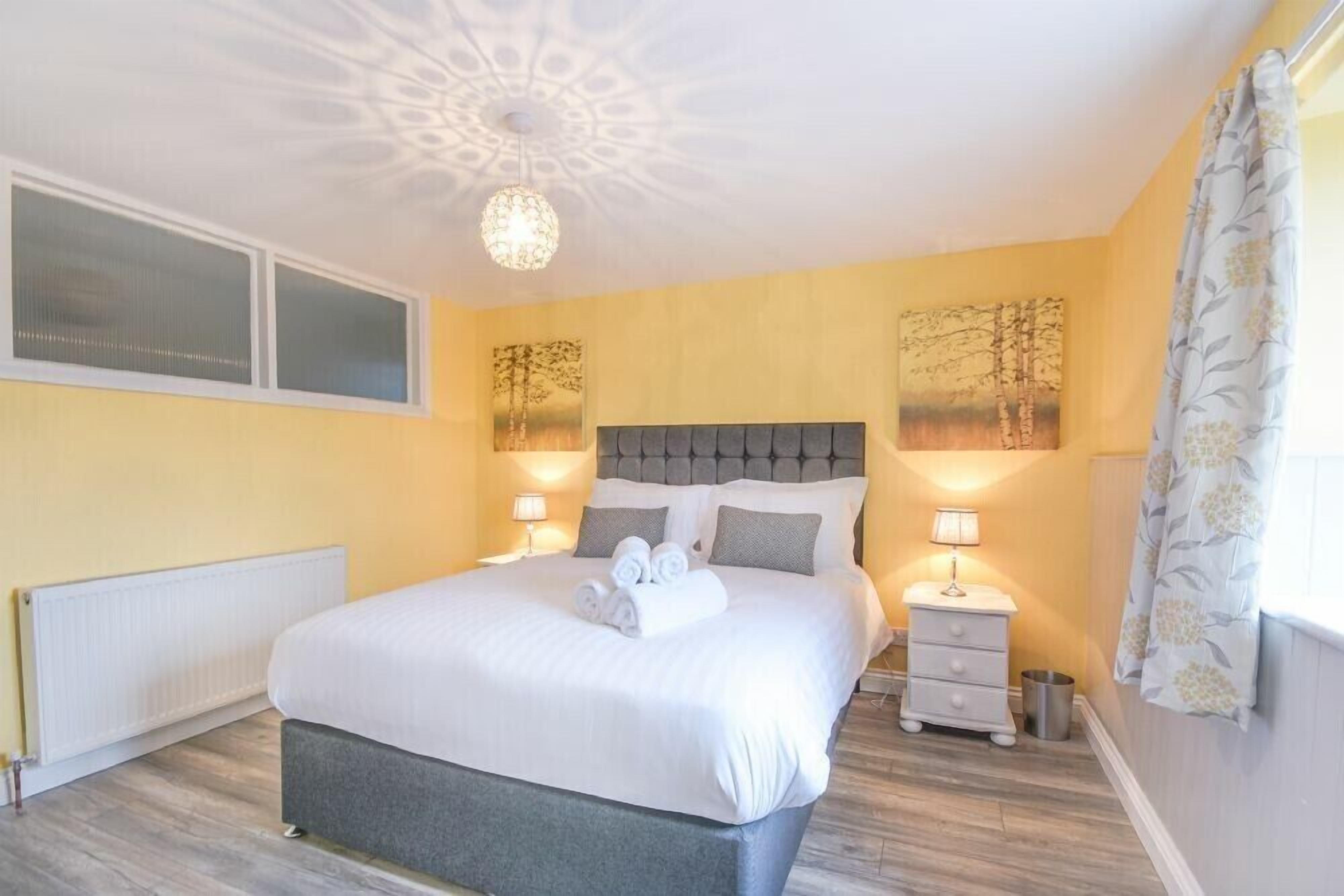 Een slaapkamer met een groot bed, nachtkastjes, een radiator en een plafondlamp.