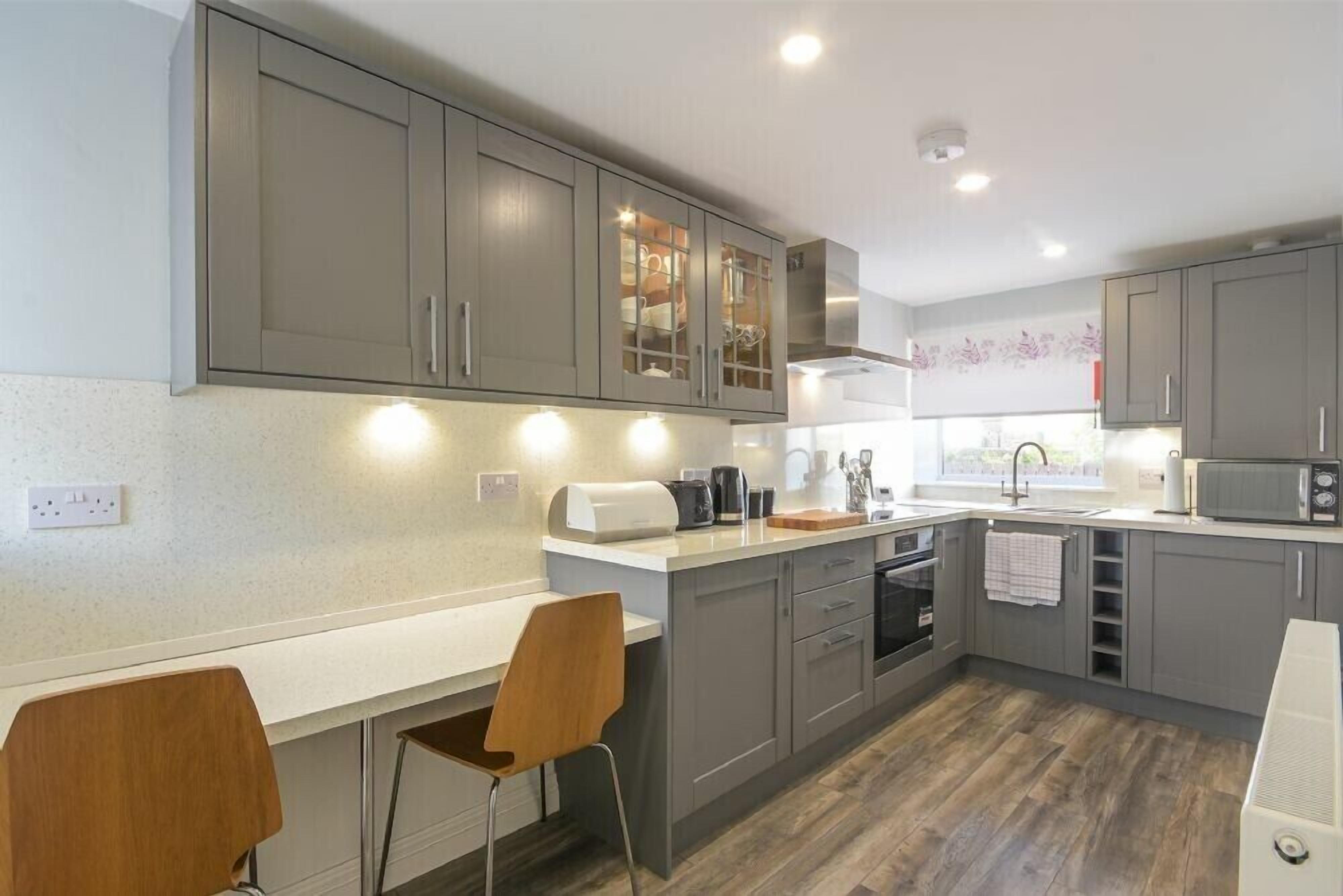 A modern kitchen with grey cabinets, a white countertop, and a wooden chair.