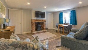 A living room with a fireplace, a television mounted on the wall, a dining area with a table and chairs, and a sofa. - Dairymaid's Cottage (Morpeth)