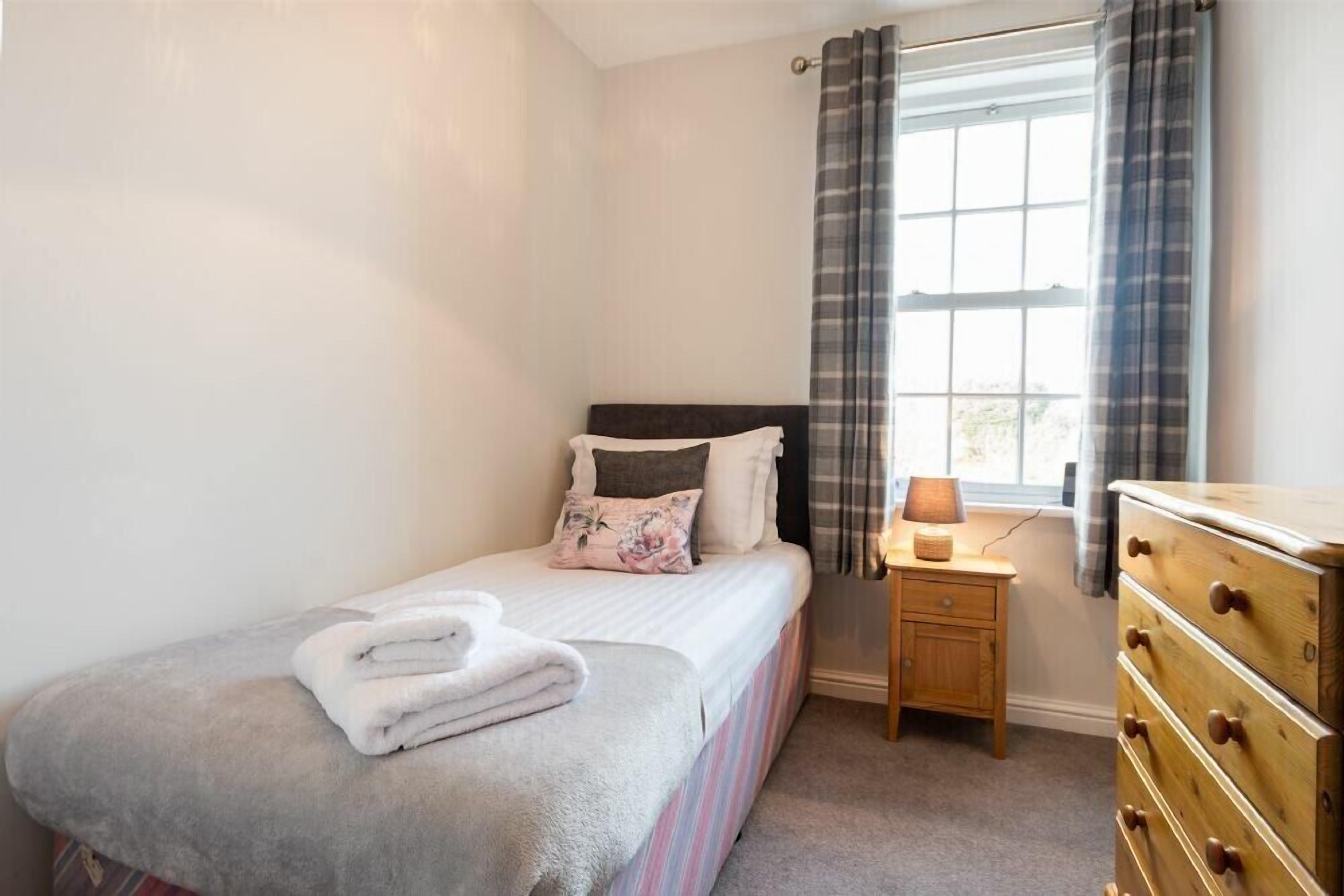 A bedroom with a bed, a nightstand, a dresser, and a window with curtains.