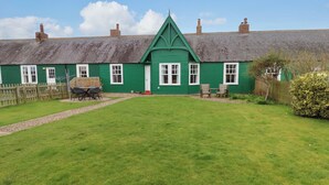 Une maison verte avec une cour gazonnée, une clôture en bois et une table entourée de chaises.