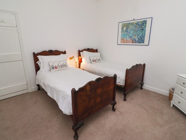 A bedroom with two wooden beds, white bedding, a white dresser, and a framed painting on the wall. - Armstrong Cottages No2 (Bamburgh)