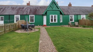 Une maison verte avec un chemin de gravier menant à une terrasse en bois.
