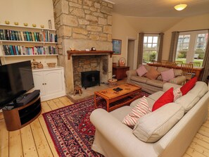 A cozy living room with a stone fireplace, a sofa set, a coffee table, and a TV. - Armstrong Cottages No2 (Bamburgh)