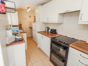 A kitchen with white cabinets, a black stove, a white refrigerator, and a wooden countertop.